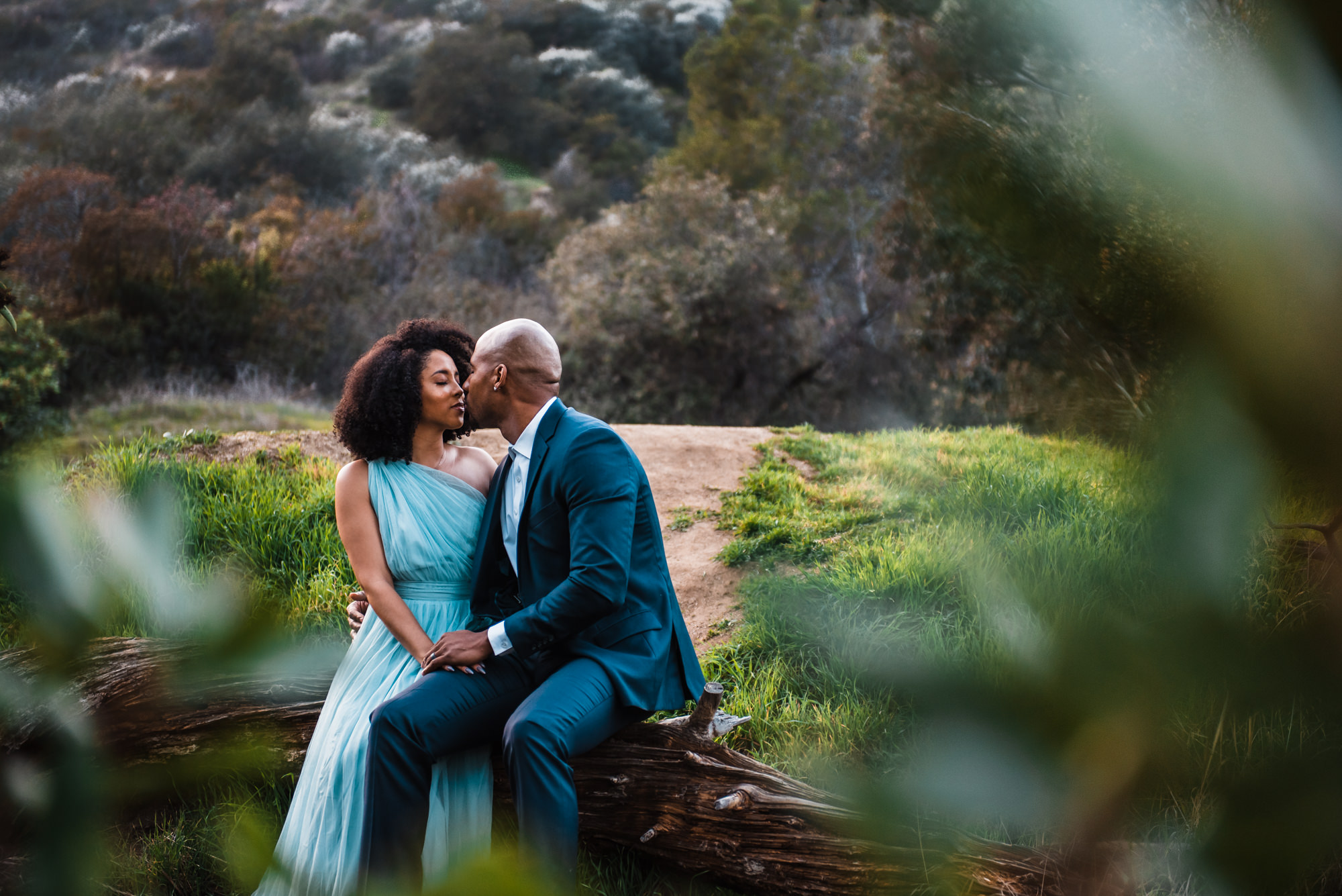 couple kisses on a fallen tree during the day of their elopement dressed in blue wedding attire