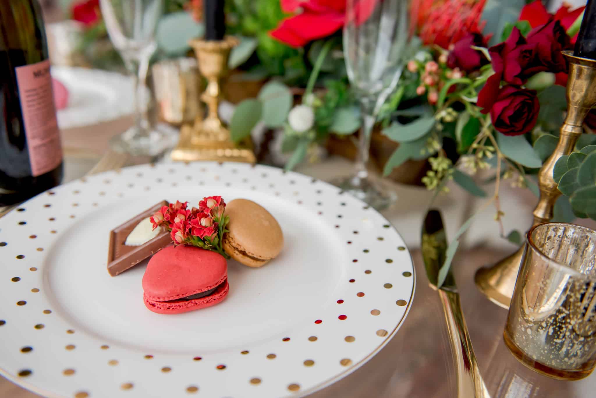 plate of two macarons and a piece of chocolate on a white and gold polka dot plate.