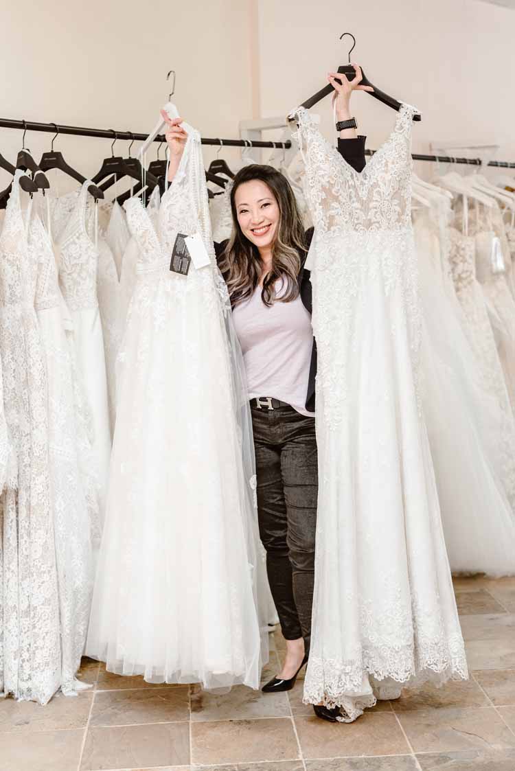 woman standing in a wedding dress store beside a rack of dressed while holding up two lace options for an intimate wedding