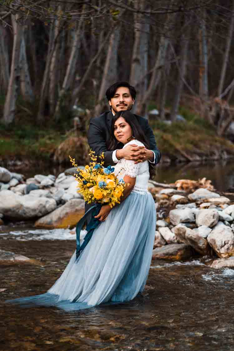 A bride and groom holding each other in a shallow river