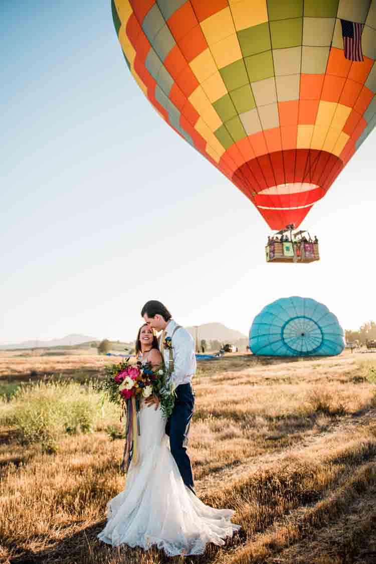 A bride and groom standing with a hot air balloon in the background