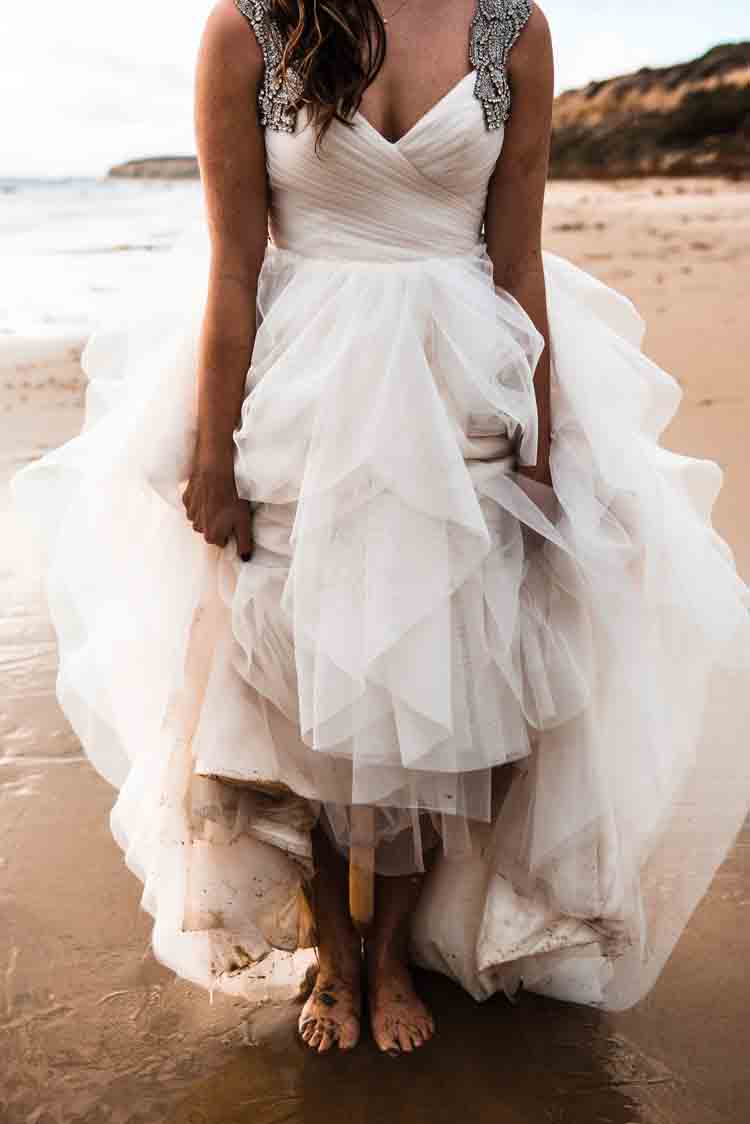 A bride holding up her dress on the beach