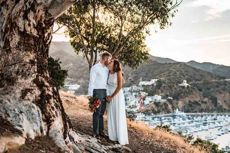 A bride and groom on a cliff with boats in the background