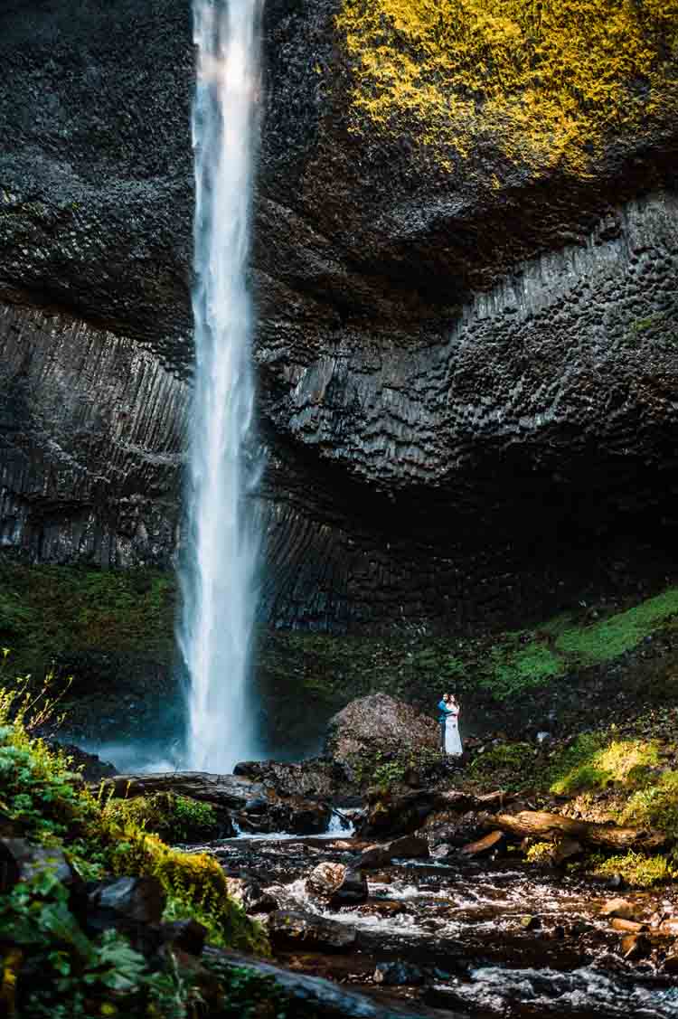 A bride and groom standing next to a waterfall
