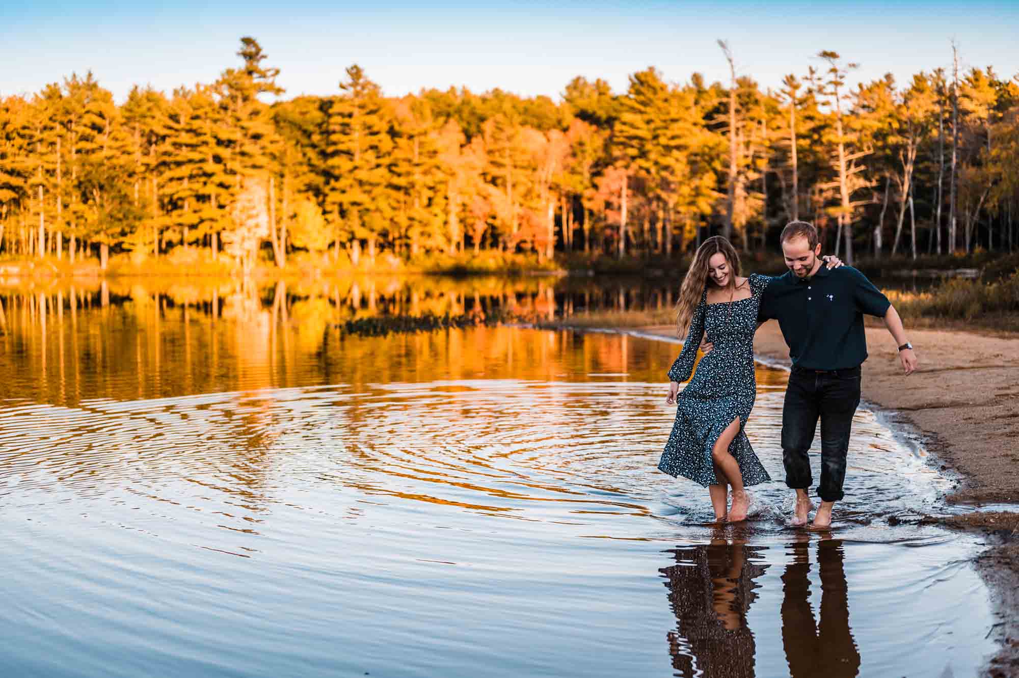 A couple dipping feet into lake in new england with forest in background