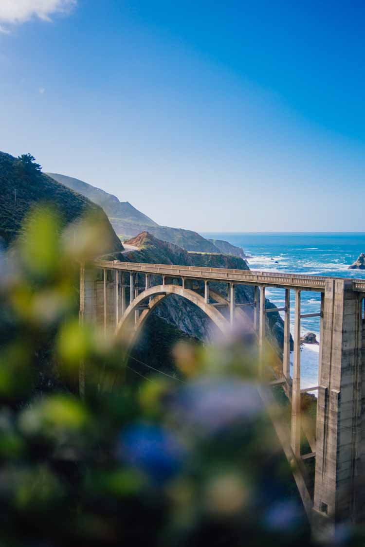 A distant shot that showcases the entirety of the Bixby Creek Bridge on a clear blue sky day which is perfect for a Big Sur elopement