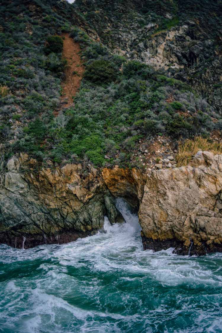 the clear blue water of Big Sur splashing up cliffside on a beautiful sunny day