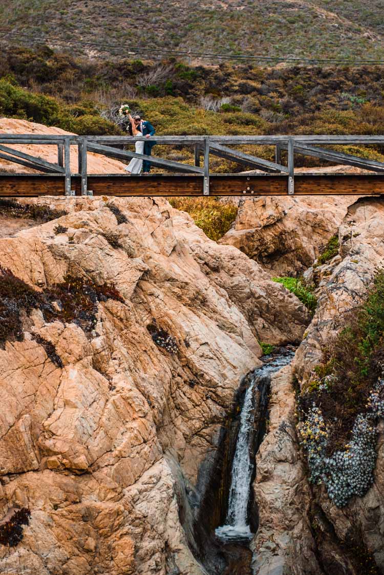 newlywed couple kissing each other on the pedestrian bridge over a waterfall in Big Sur California