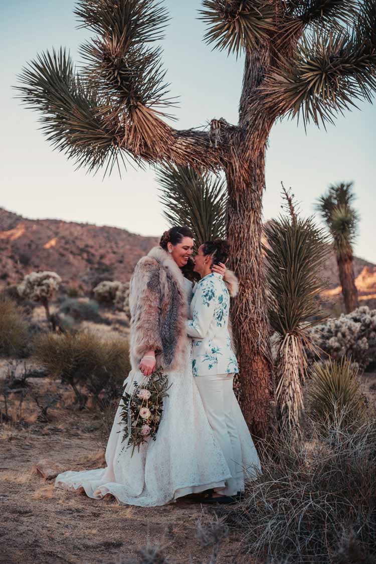 newlywed couple stands in front of a cactus smiling and looking into one another's eyes