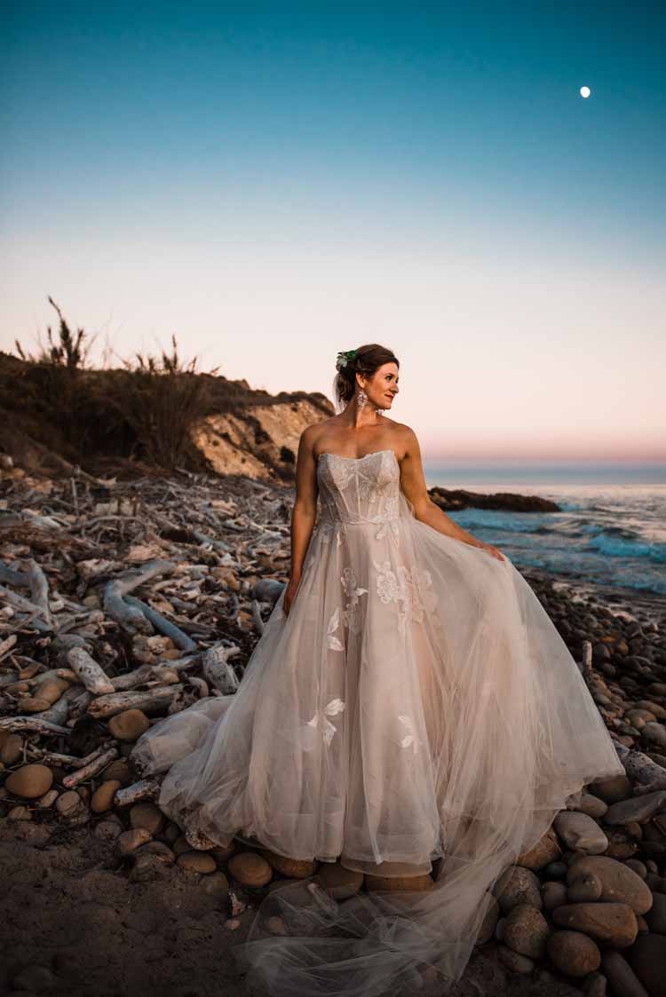 bride standing on the beach in her off-white detailed elopement wedding dress at sunset