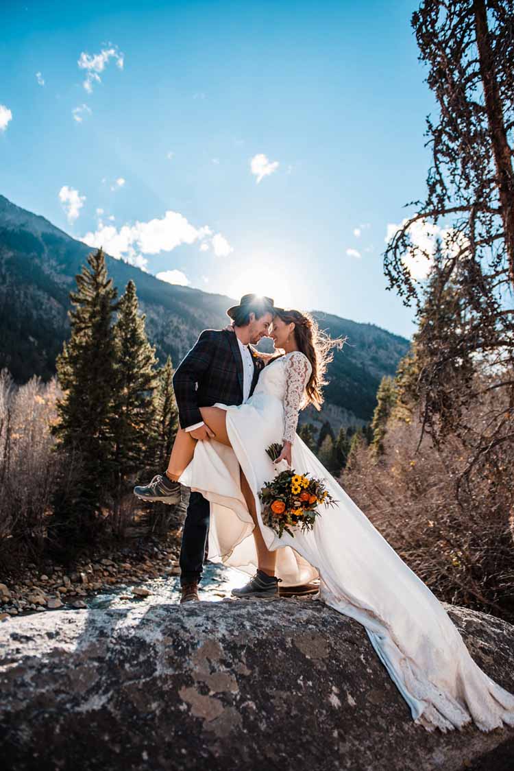 husband holds up one leg of his bride and holds her close while she smiles in her long-train wedding dress and hiking boots
