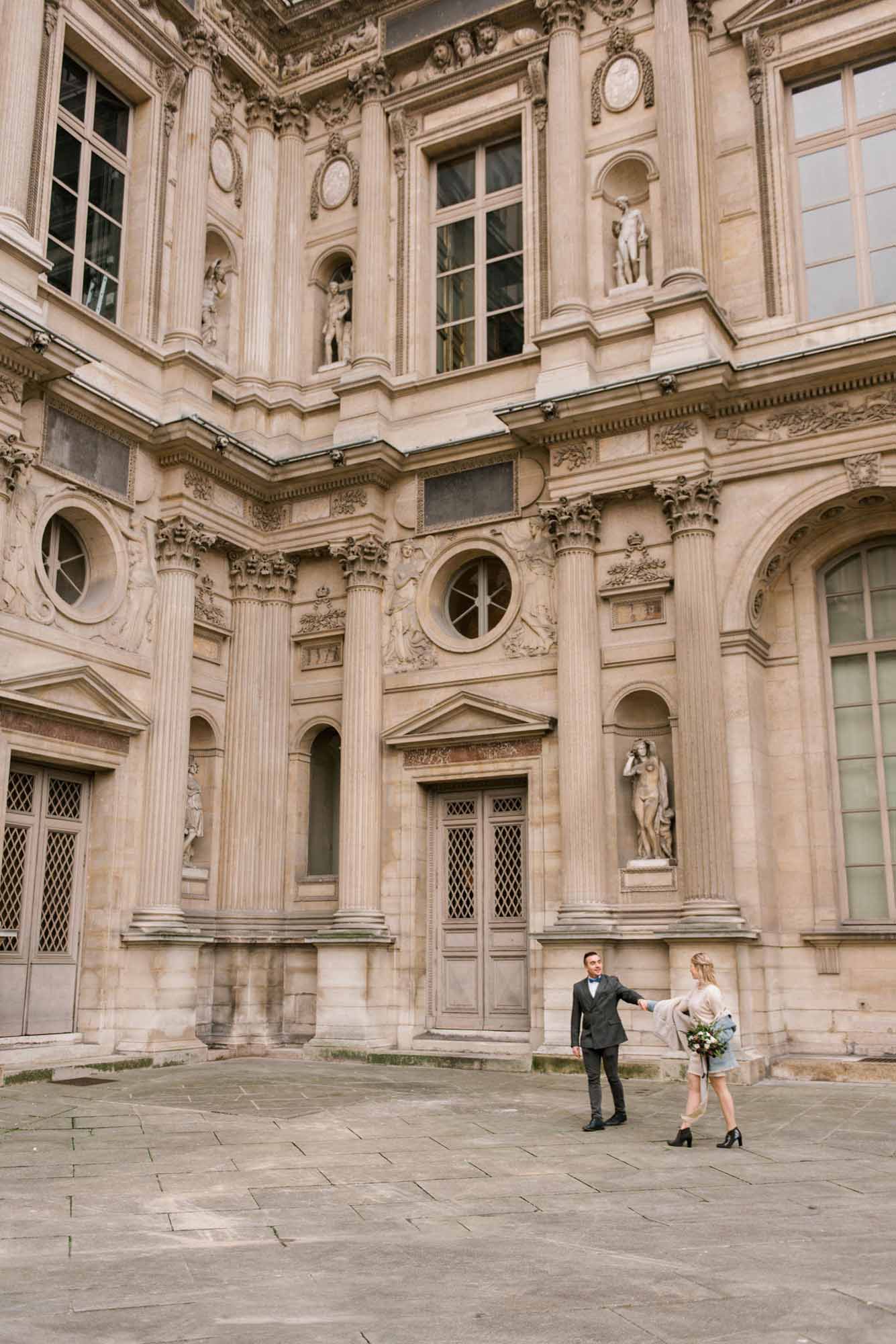 young couple strolls holding hands in front of an old building for their Paris engagement during the winter