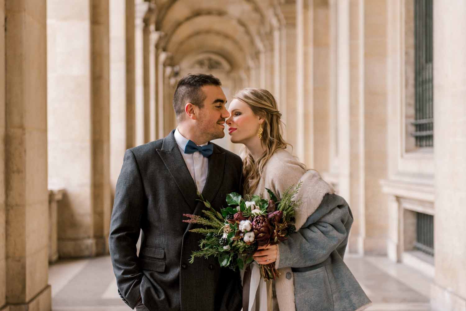 couple stands under grande building archway leaning in for a kiss following their engagement in Paris