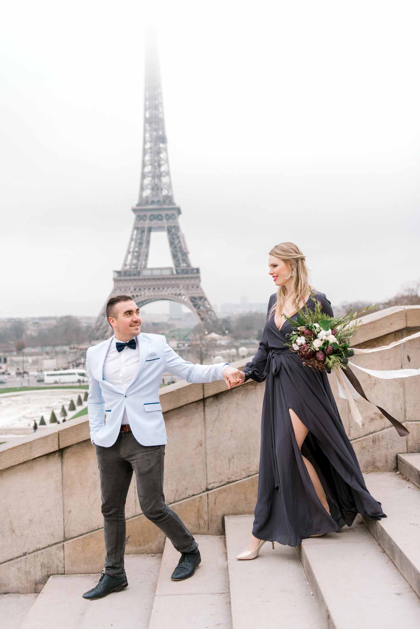 newly engaged couple walks down steps in Paris with the Eiffel Tower in the background during winter time