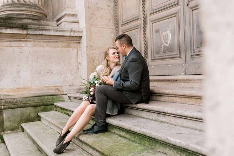 newly engaged young couple sits together on the stairs of an old building in Paris