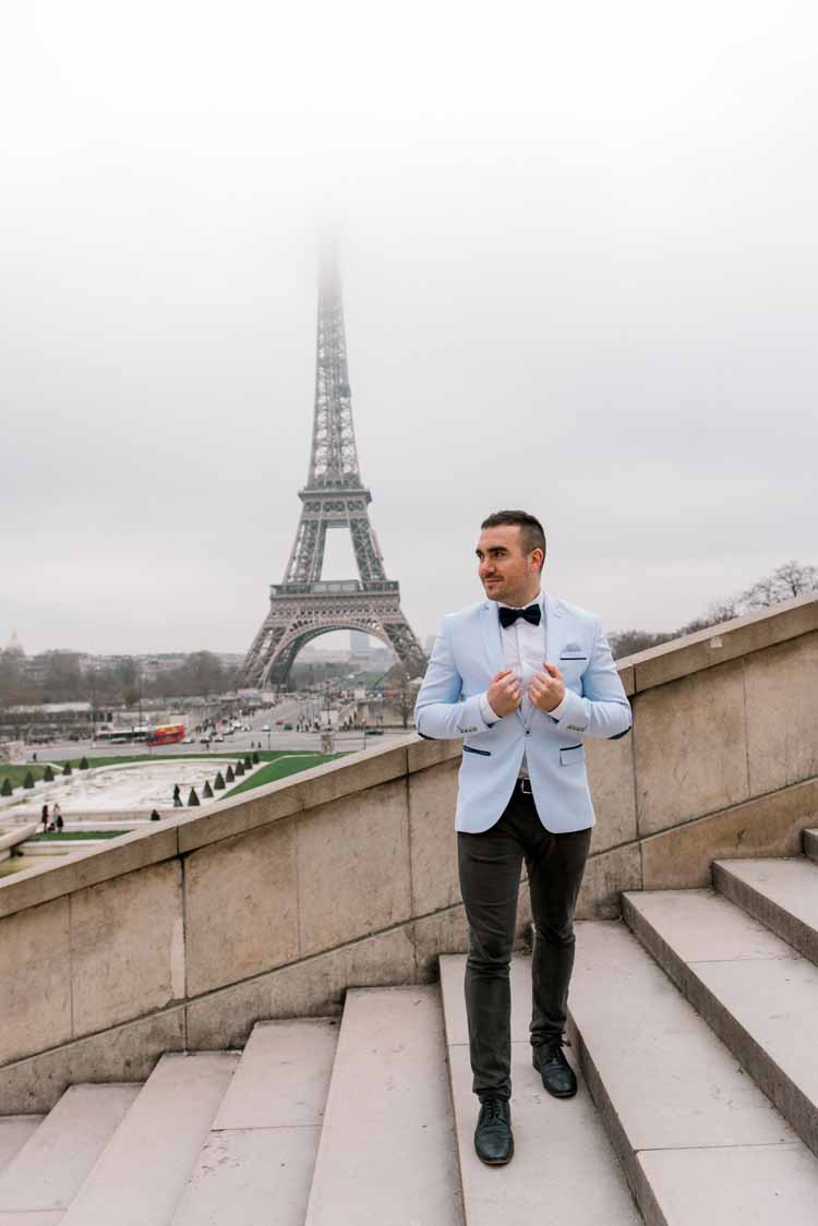 young man stands in a light blue blazer jacket in Paris during winter to celebrate his engagement