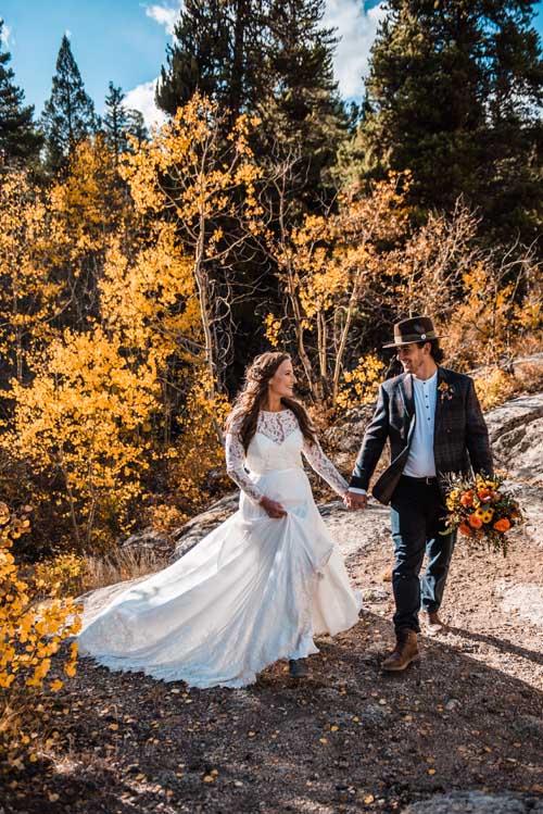 A bride and groom smiling at each other while walking in the forest during an elopement with yellow trees in the background