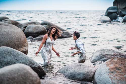 A bride and groom smiling while playing on a rocky beach shore during an elopement