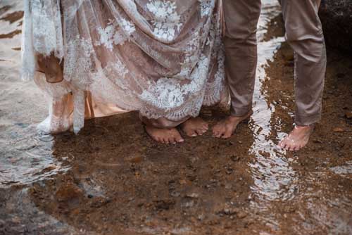 The feet of a bride and groom standing on the shallow part of a lake during an elopement