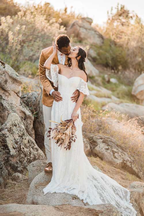A groom standing behind a bride while standing on a rock kissing during an elopement