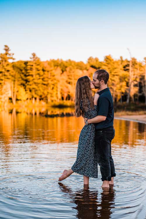A bride and groom kissing during an elopement on a lake with yellow trees in the background