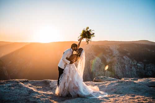 A bride and groom kissing on the top of a cliff during a yosemite sunrise elopement