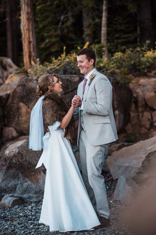 A bride and groom holding hands and laughing while standing on small rocks during an elopement