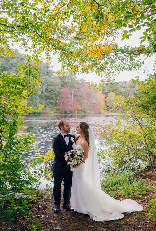 A bride and groom embracing each other surrounded by green branches with a lake in the background during an elopement