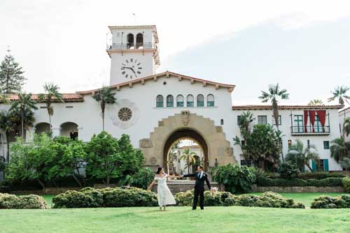 A bride and groom holding hands during an elopement on a green lawn with a resort in the background