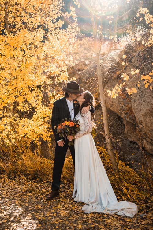 A bride and groom kissing in a forest of yellow trees during an elopement