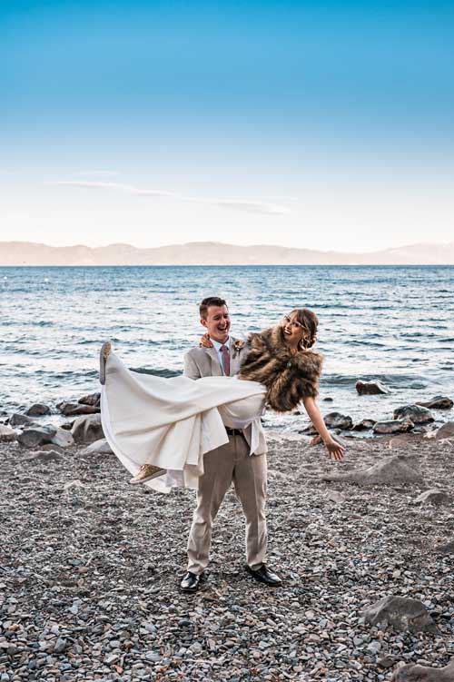 A groom carrying a bride on the beach shore during an elopement