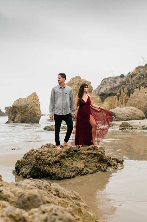A bride and groom on top of a rock on the beach shore during an elopement