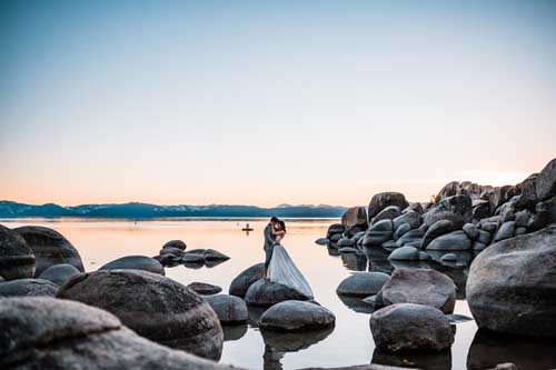 A bride and groom standing on rocks on a shallow lake during an elopement