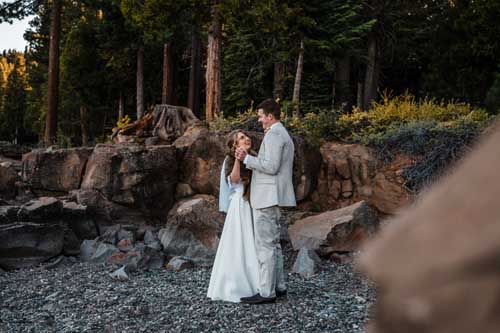 A couple standing on small rocks looking at each other while smiling and holding hands during a lake tahoe elopement