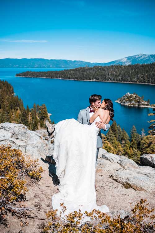 A groom carrying a bride during an elopement on top of a cliff with lake tahoe in the background
