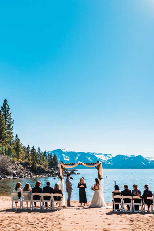 A couple being married during an elopement with family sitting by and lake tahoe in the background